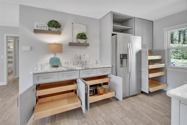 kitchen with light wood-style floors, light stone counters, open shelves, and stainless steel refrigerator with ice dispenser