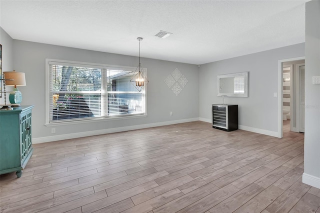 unfurnished dining area featuring a textured ceiling, light wood-type flooring, visible vents, and baseboards