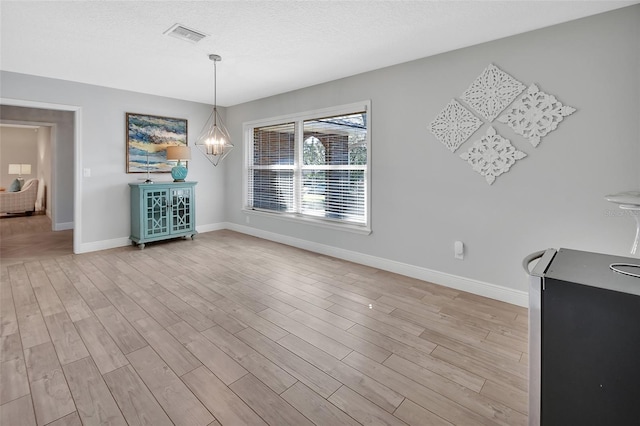 unfurnished dining area featuring a notable chandelier, visible vents, light wood-style flooring, a textured ceiling, and baseboards