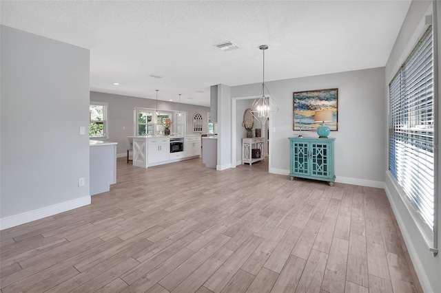 unfurnished living room with visible vents, baseboards, a textured ceiling, light wood-type flooring, and a notable chandelier