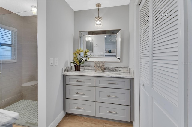 bathroom with a tile shower, vanity, baseboards, and wood finished floors