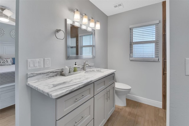 bathroom with visible vents, toilet, vanity, wood finished floors, and baseboards