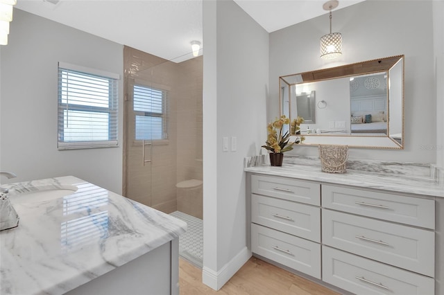 bathroom with baseboards, wood finished floors, tiled shower, and vanity