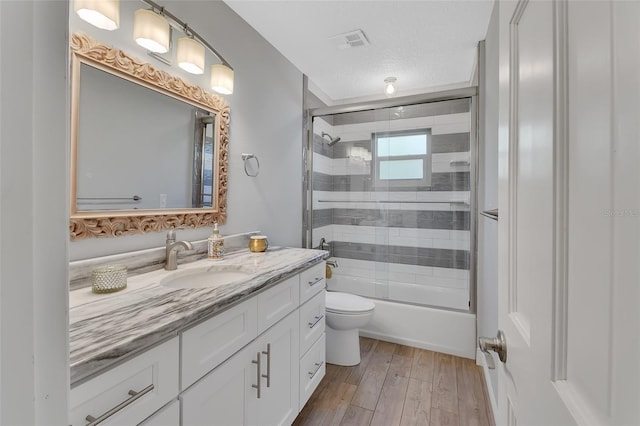 full bathroom featuring shower / bath combination with glass door, visible vents, toilet, vanity, and wood finished floors