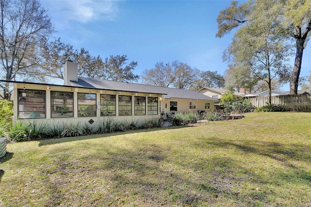 rear view of house featuring a yard, a chimney, and fence