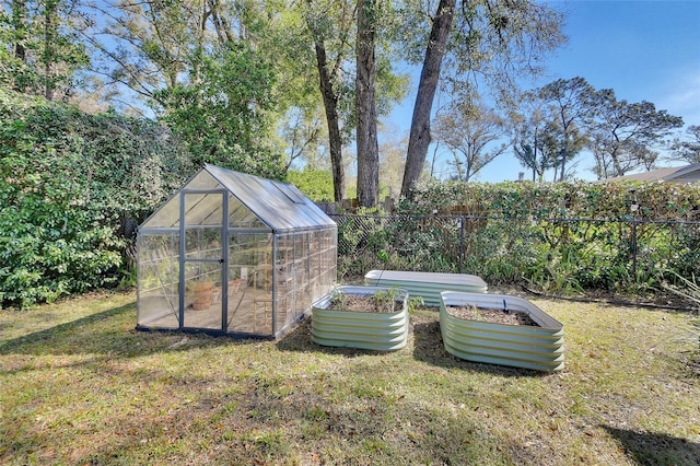 view of yard featuring an outdoor structure, a greenhouse, fence, and a garden