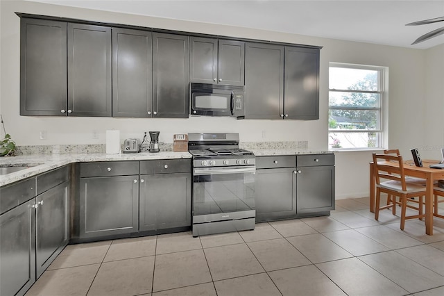 kitchen with black microwave, stainless steel gas range, light tile patterned flooring, and light stone countertops