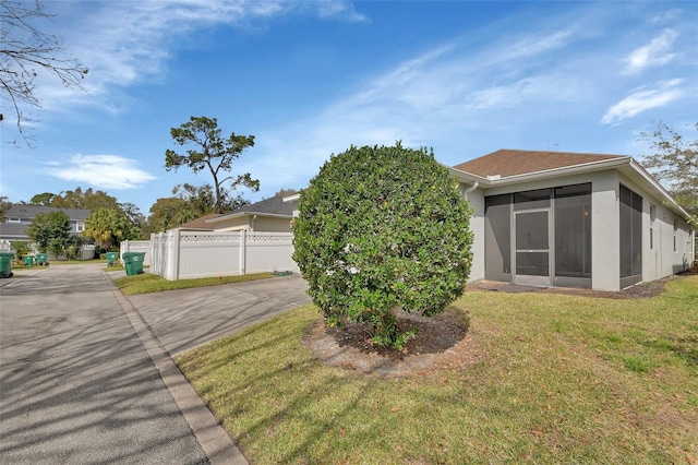 view of front of house featuring stucco siding, a sunroom, fence, driveway, and a front lawn