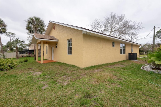 rear view of property featuring central AC, a lawn, and stucco siding