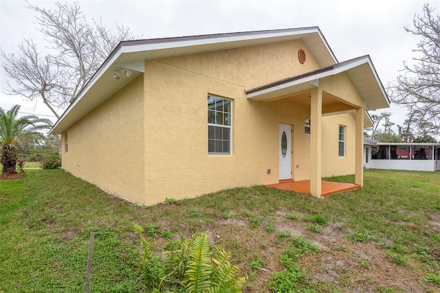 back of property featuring a sunroom, a lawn, and stucco siding