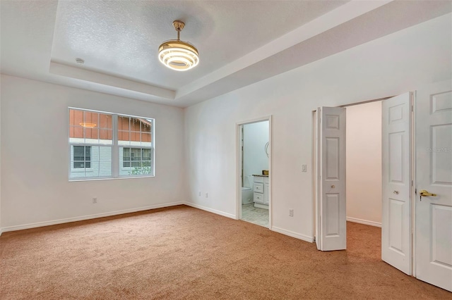 unfurnished bedroom featuring a textured ceiling, a tray ceiling, carpet, and baseboards