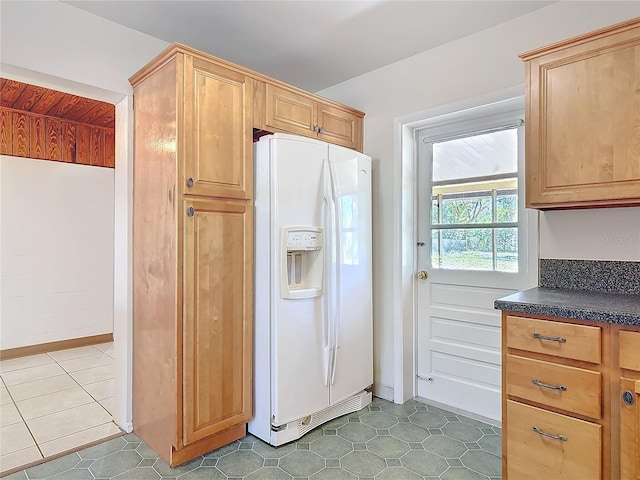 kitchen featuring light brown cabinetry, white refrigerator with ice dispenser, dark countertops, and tile patterned flooring