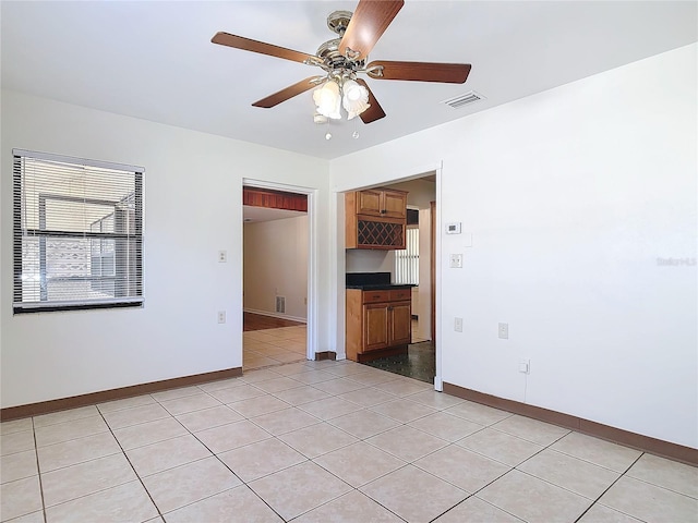 spare room featuring a ceiling fan, visible vents, baseboards, and light tile patterned floors