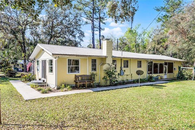 rear view of property featuring metal roof, a lawn, a chimney, and central air condition unit