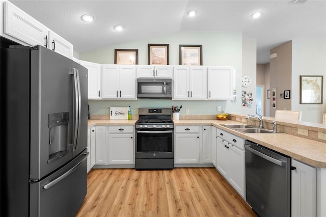 kitchen with white cabinets, lofted ceiling, appliances with stainless steel finishes, light countertops, and a sink