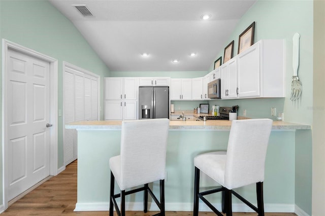 kitchen featuring a breakfast bar, light countertops, appliances with stainless steel finishes, vaulted ceiling, and a peninsula