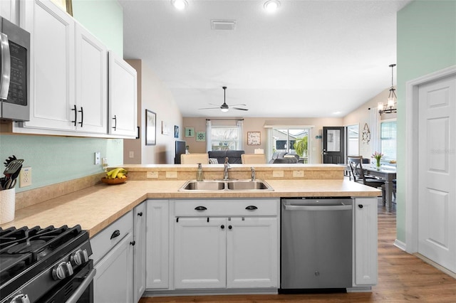 kitchen with stainless steel appliances, a peninsula, a sink, visible vents, and white cabinetry