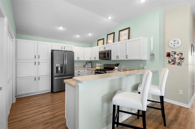 kitchen featuring stainless steel appliances, a breakfast bar, a peninsula, white cabinets, and light countertops