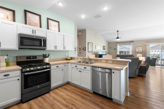 kitchen with appliances with stainless steel finishes, a peninsula, vaulted ceiling, light countertops, and a sink