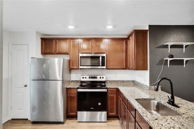 kitchen featuring light stone counters, a sink, appliances with stainless steel finishes, open shelves, and light wood finished floors