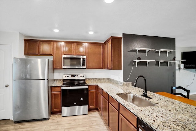 kitchen featuring stainless steel appliances, light stone counters, a sink, and light wood-style flooring