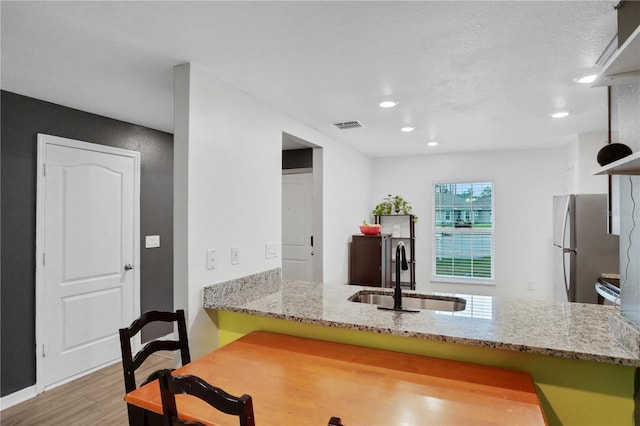 kitchen featuring visible vents, wood finished floors, freestanding refrigerator, a peninsula, and a sink