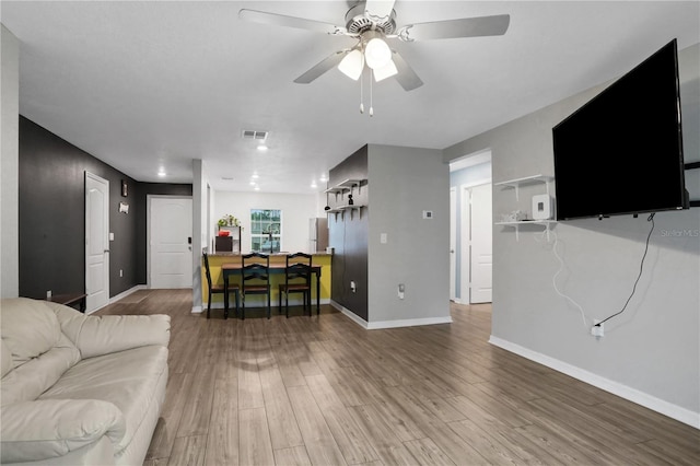 living area featuring a ceiling fan, visible vents, baseboards, and wood finished floors