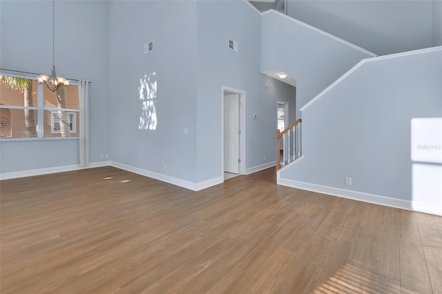 unfurnished living room featuring a healthy amount of sunlight, an inviting chandelier, stairway, and wood finished floors