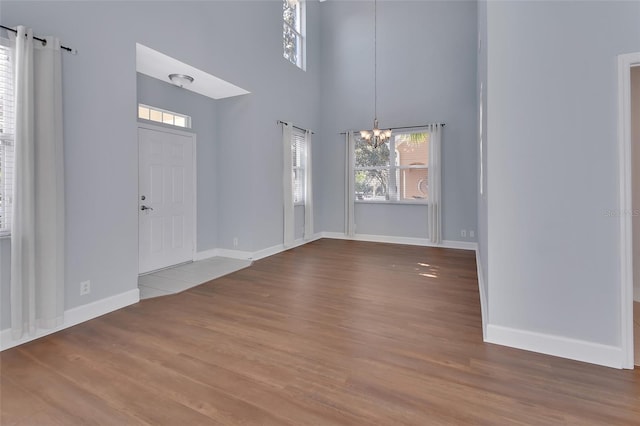 foyer entrance featuring baseboards, wood finished floors, a towering ceiling, and a notable chandelier