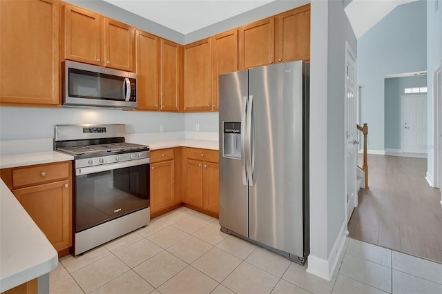 kitchen with light tile patterned floors, baseboards, appliances with stainless steel finishes, and light countertops