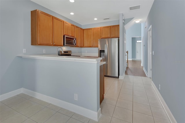 kitchen with light tile patterned floors, a peninsula, visible vents, light countertops, and appliances with stainless steel finishes