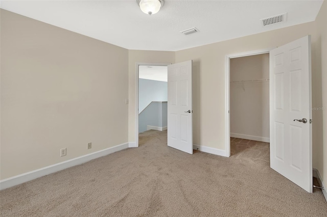 unfurnished bedroom featuring light carpet, a spacious closet, visible vents, and baseboards