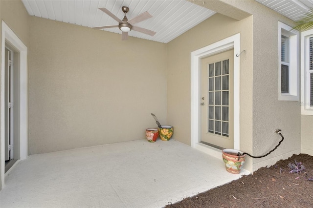 entrance to property with a ceiling fan and stucco siding