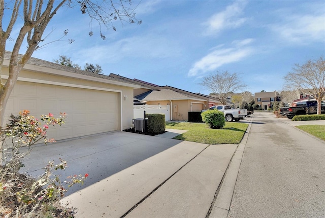 exterior space featuring stucco siding, concrete driveway, central AC, fence, and a residential view