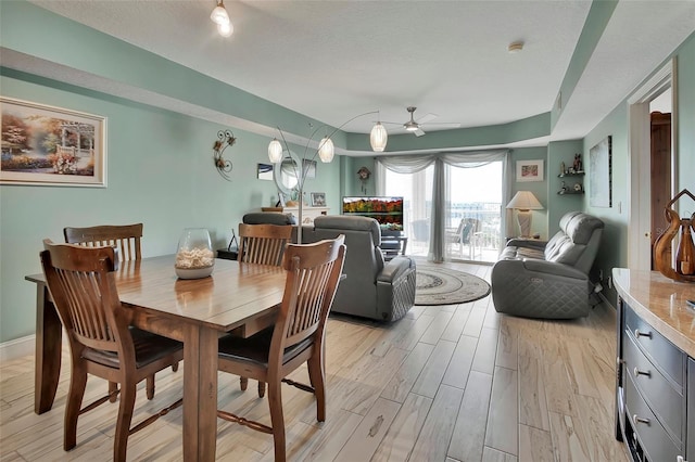 dining area featuring a ceiling fan, baseboards, light wood-style flooring, and a textured ceiling