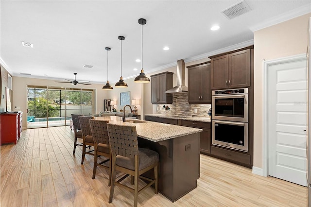 kitchen featuring wall chimney exhaust hood, visible vents, a sink, dark brown cabinets, and a kitchen bar