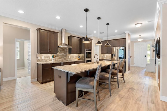 kitchen with wall chimney exhaust hood, appliances with stainless steel finishes, a breakfast bar area, and dark brown cabinetry