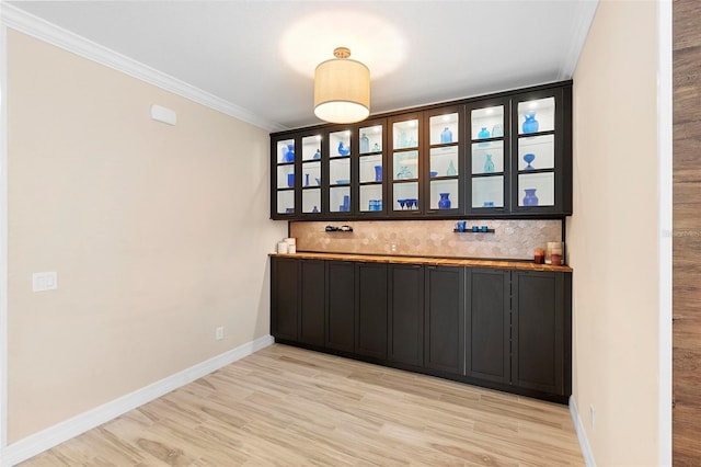 bar with light wood-style flooring, ornamental molding, backsplash, and baseboards