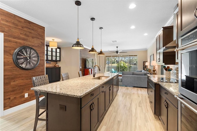 kitchen with ornamental molding, a sink, dark brown cabinetry, and wooden walls