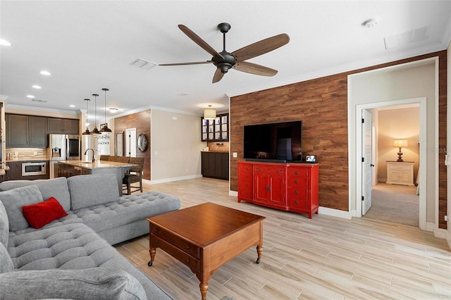 living room with ceiling fan, an accent wall, baseboards, light wood finished floors, and crown molding