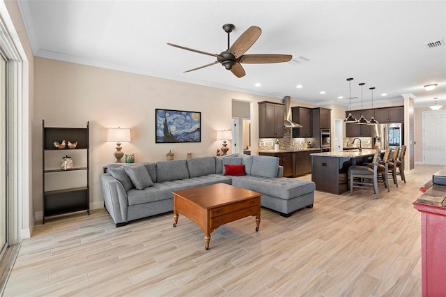 living area featuring recessed lighting, visible vents, light wood-style flooring, ornamental molding, and a ceiling fan