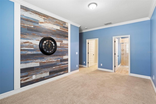 unfurnished bedroom with an accent wall, carpet, visible vents, and ornamental molding