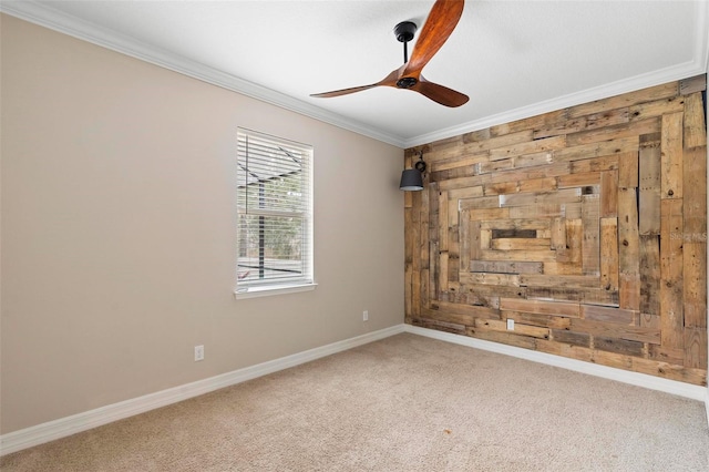 empty room featuring light carpet, wooden walls, baseboards, ceiling fan, and crown molding