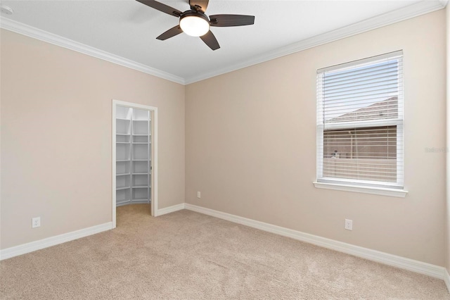 spare room featuring a ceiling fan, light colored carpet, crown molding, and baseboards