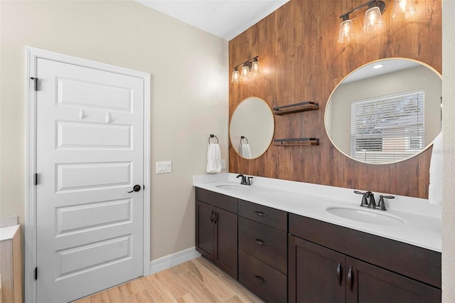 full bath with double vanity, wood finished floors, a sink, and baseboards