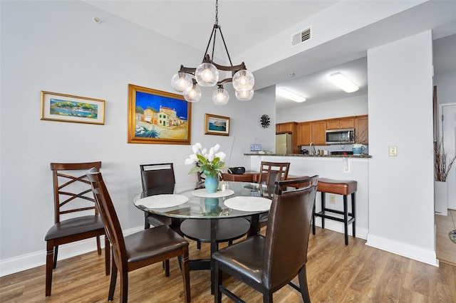 dining space featuring light wood-type flooring, visible vents, baseboards, and an inviting chandelier