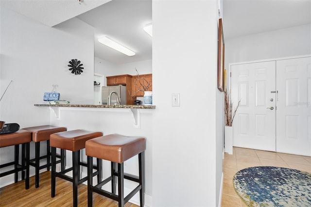 kitchen featuring light tile patterned floors, a kitchen breakfast bar, stainless steel refrigerator with ice dispenser, brown cabinets, and dark stone countertops