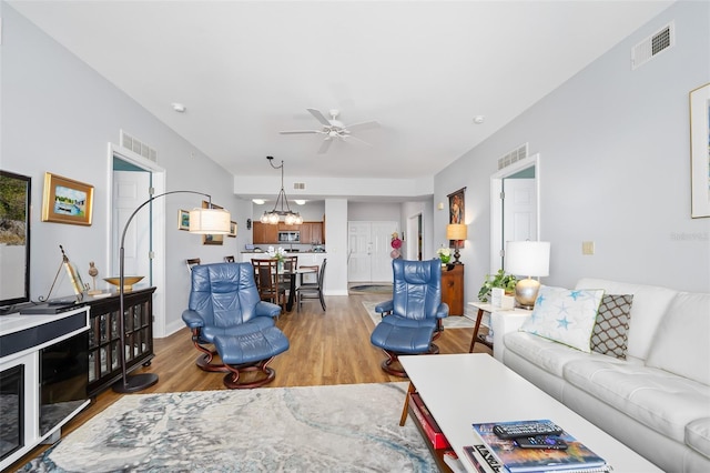 living area featuring ceiling fan with notable chandelier, wood finished floors, and visible vents