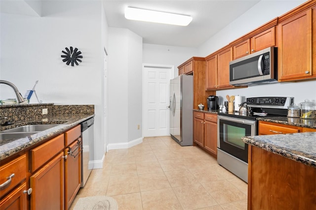 kitchen featuring dark stone counters, stainless steel appliances, a sink, and brown cabinets