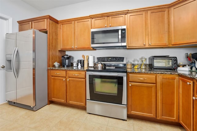 kitchen featuring appliances with stainless steel finishes, brown cabinetry, and dark stone countertops